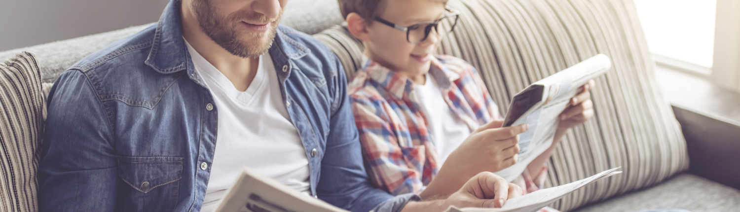 Father And Son Are Reading Newspapers And Smiling Spending Time Together on Couch