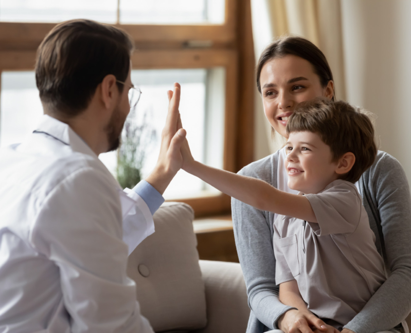 Little boy sits on moths lap while doctor gives him a high-five