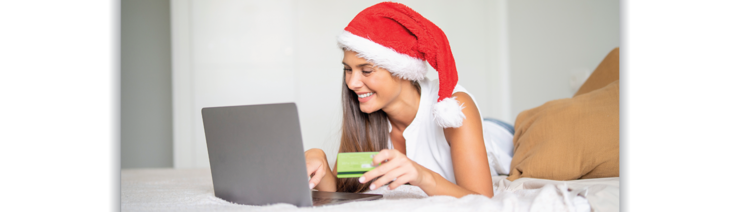 Woman wearing a Santa hat looking at a laptop with credit card in hand.