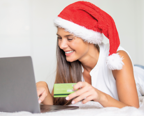 Woman wearing a Santa hat looking at a laptop with credit card in hand.